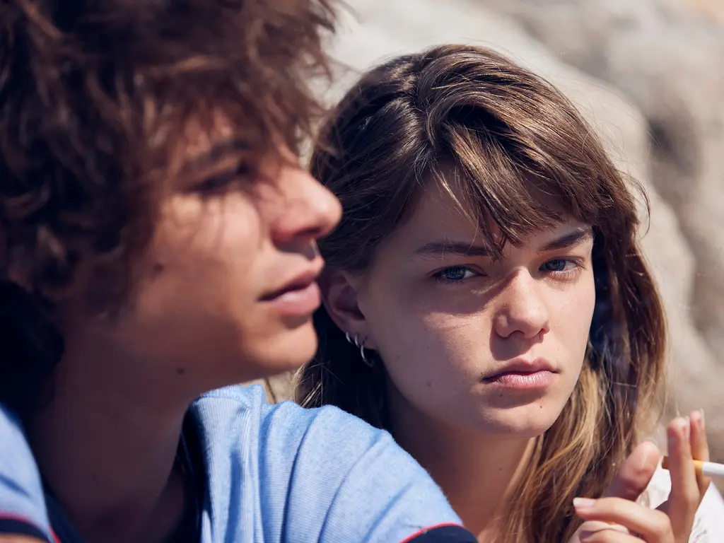 Two people, a young man and woman, with serious expressions, looking intently at each other.